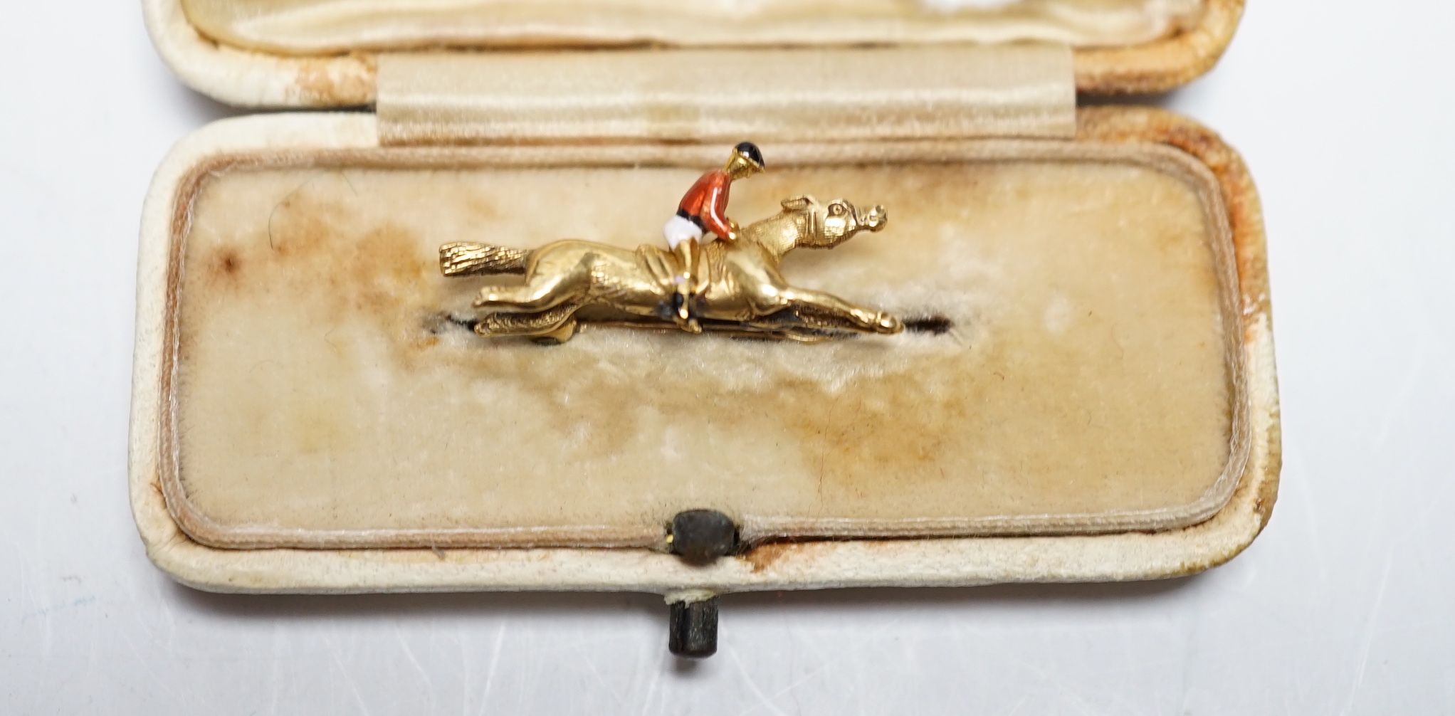 An Edwardian yellow metal, and polychrome enamelled novelty brooch, modelled as a horse with jockey, 25mm, gross weight 3,8 grams.